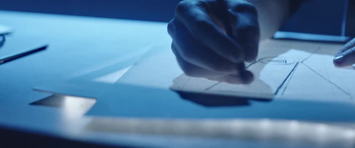 A person sitting in a room at a desk drawing with a pen on a paper
