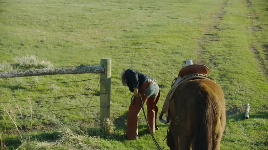 A middle aged cowboy opens a gate to let his horse into pasture as he wraps up a long day of work on the bison ranch