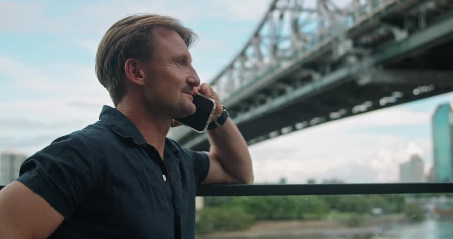 A man is talking on his cell phone by the bridge