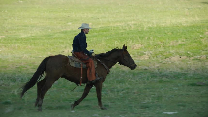Slow motion tight shot of a cowboy riding a brown horse in a wide open green valley in Blue Sky Country Montana