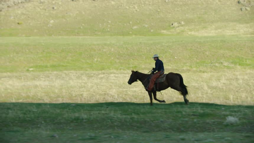 Silhouette slow motion shot of a cowboy riding a brown horse at sunset in beautiful Montana
