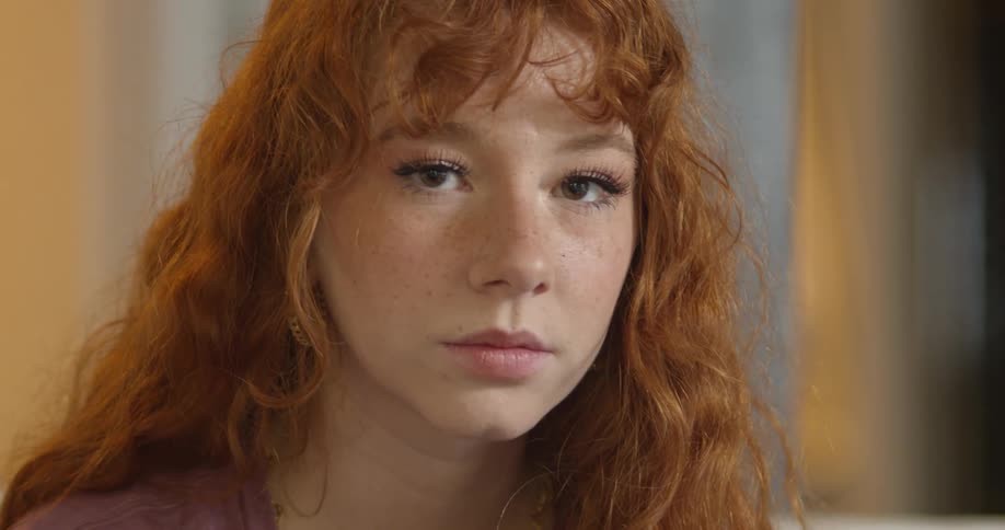 A woman with earrings in a room staring with a wall in the background