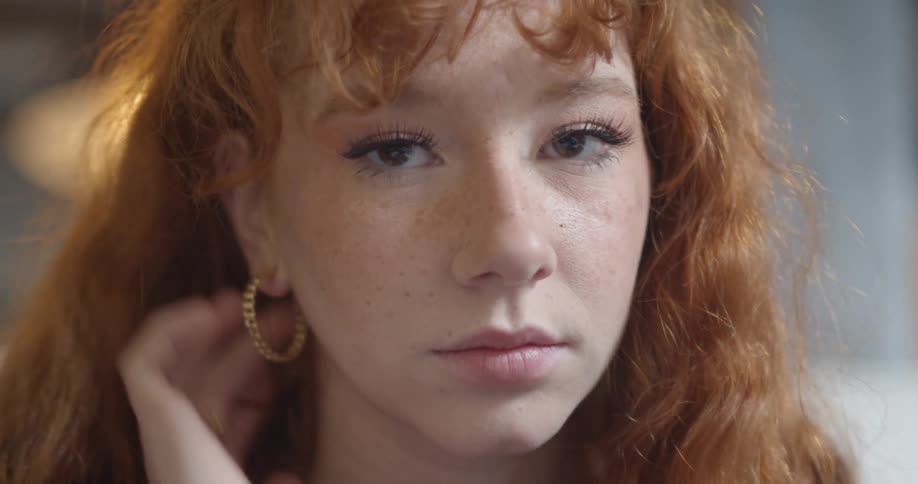 A young woman tucking her red hair behind her ear while posing