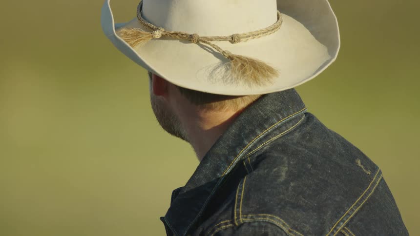 Square jawed cowboy with a beard a tan cowboy hat and a denim jacket contemplates life on a bison ranch in Montana