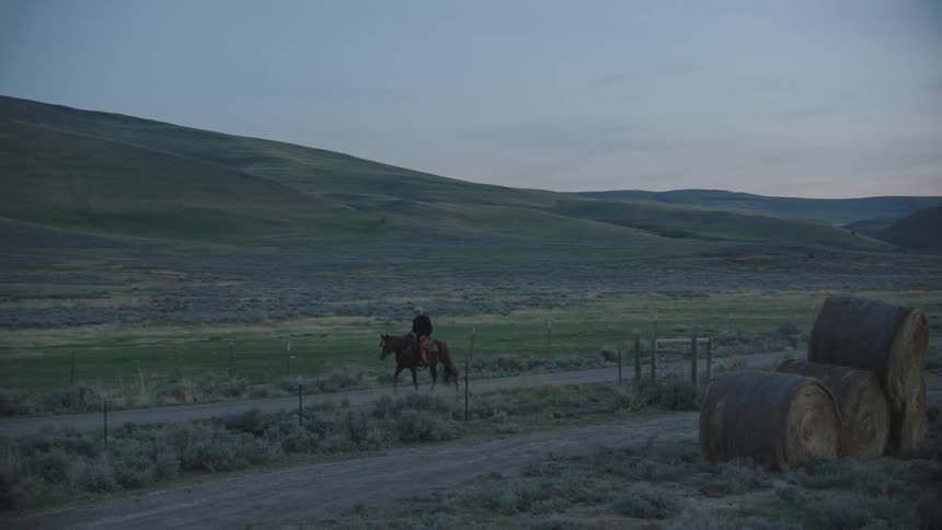 A cowboy riding a horse with hills the sky and clouds in the background in pre sunrise light during the blue hour quiet time of day before the hard work begins