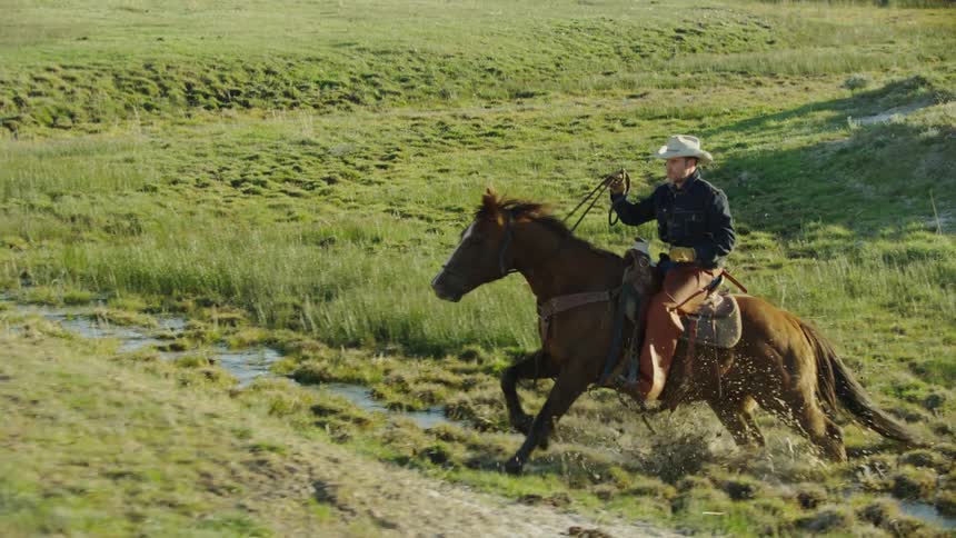 Slow motion shot of a man riding a brown horse through a muddy creek in rural Montana
