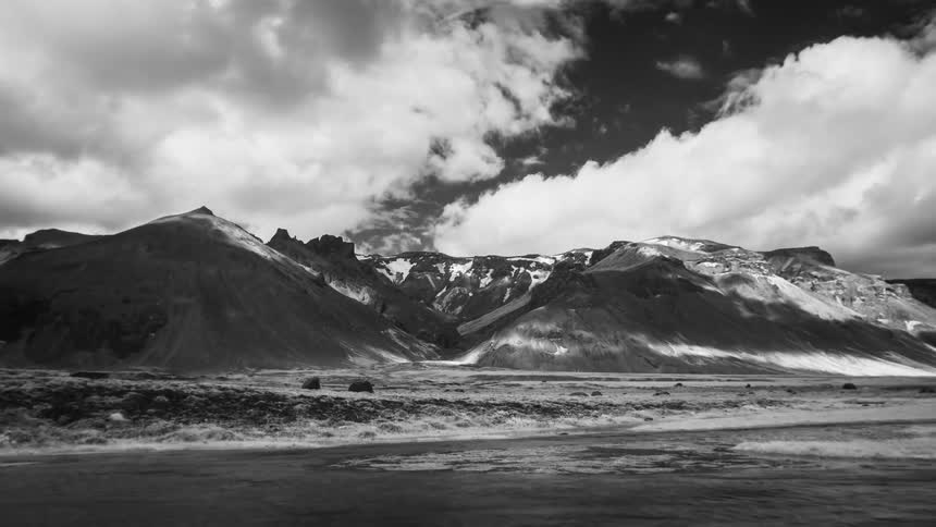 A landscape with a river and a mountain range with the sky and clouds in the background