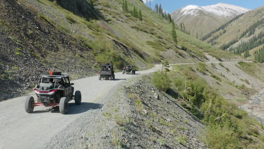 Vehicles driving on a dirt road with a mountain range the sky and clouds in the background
