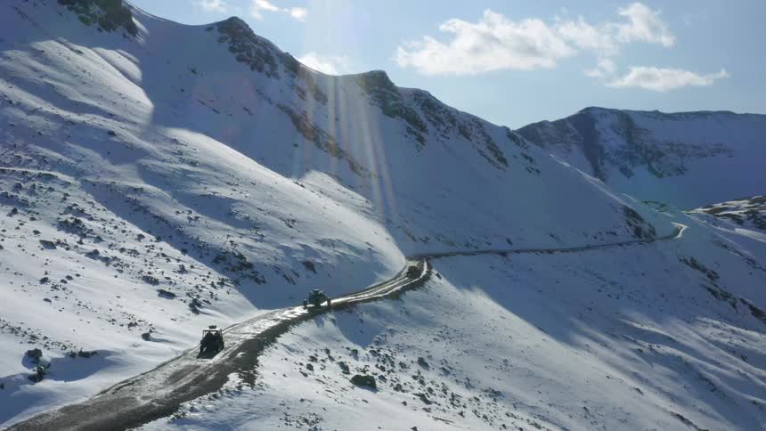 Three vehicles travel on a mountain road on a bright sunny day