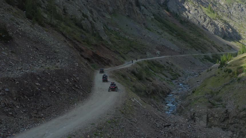 A group of dune buggies travel a cliffside dirt road