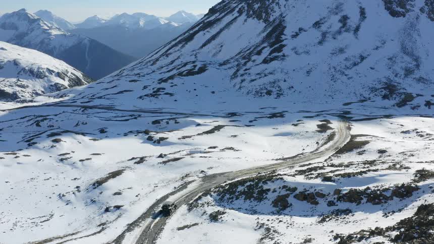 Black truck travels on a road alongside snow covered mountains and a mountain range on the horizon