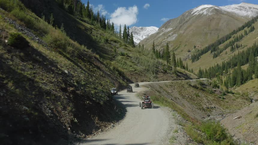 Dune buggies drive along a dirt road in the valley of a mountain