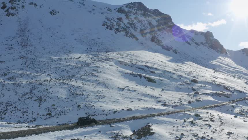 Black truck travels down a road alongside snow covered mountains