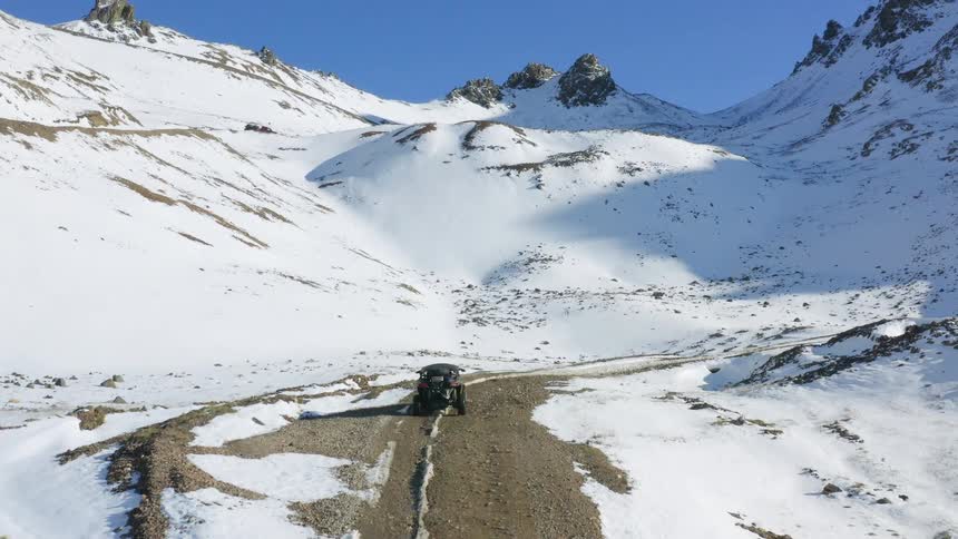 An aerial view of a car traveling on a dirt road in snowy mountains