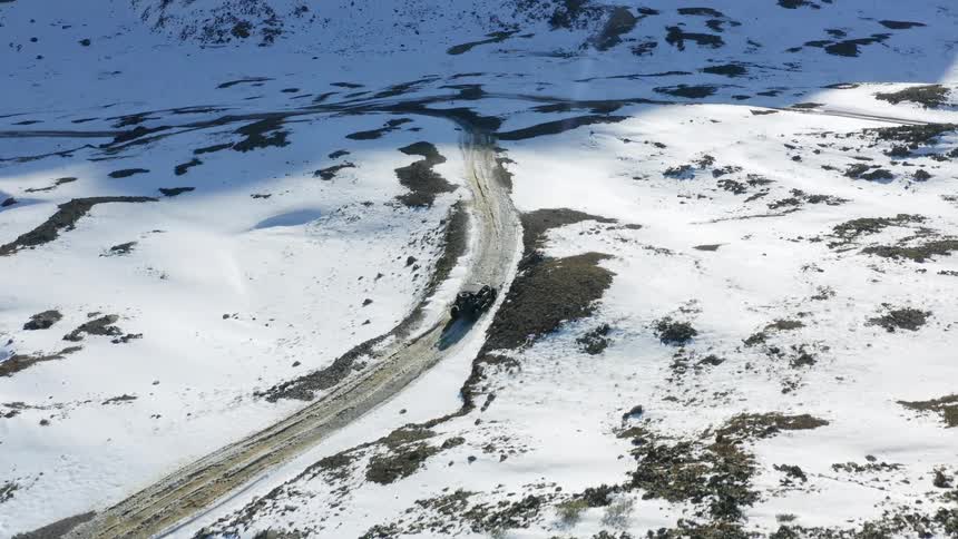 Black truck travels down a road with snow all around