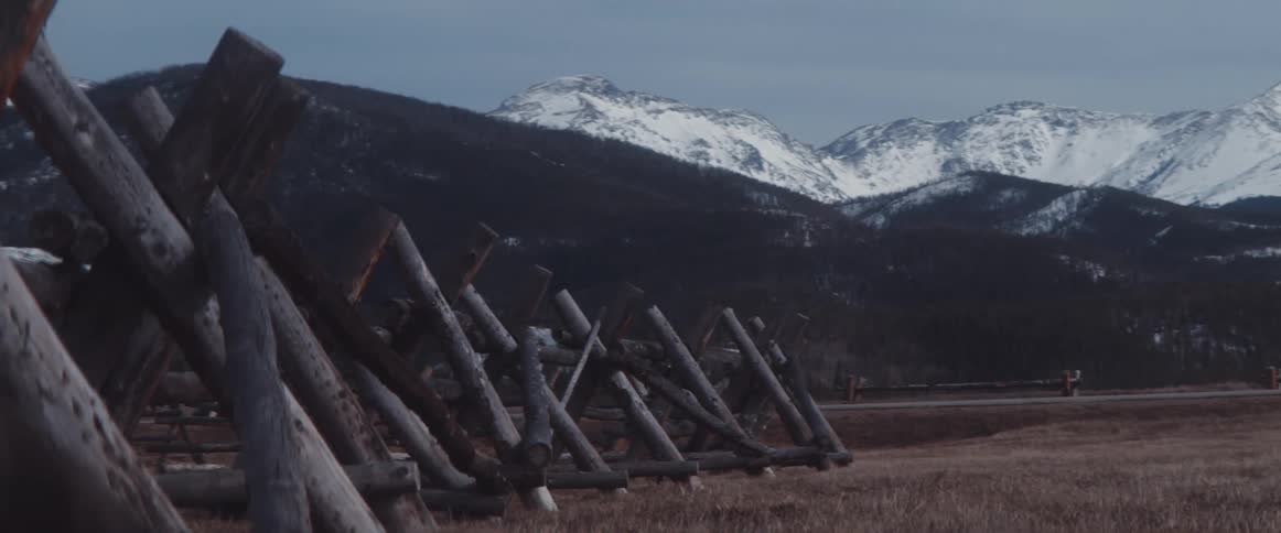 Wooden barricades in a field below a snowy mountain range during the day
