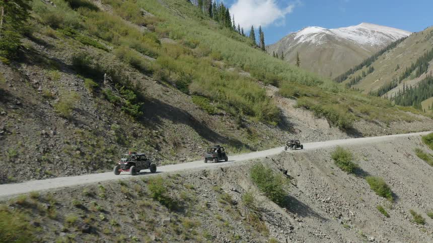 Vehicles driving on a dirt road with a mountain range the sky and clouds in the background