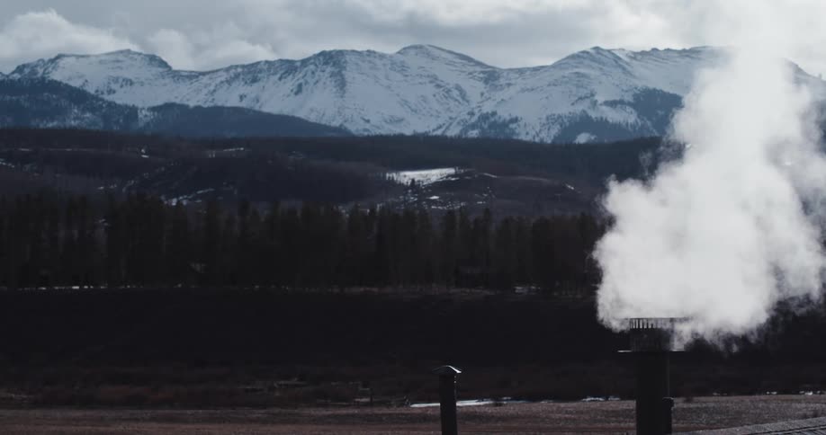 Steam billowing from a vent with snowy mountains in the distance