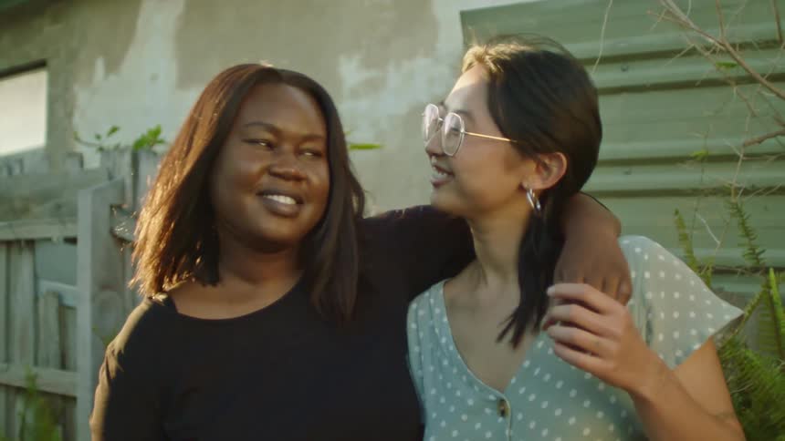 Two female friends standing outside a house smile while looking at the camera