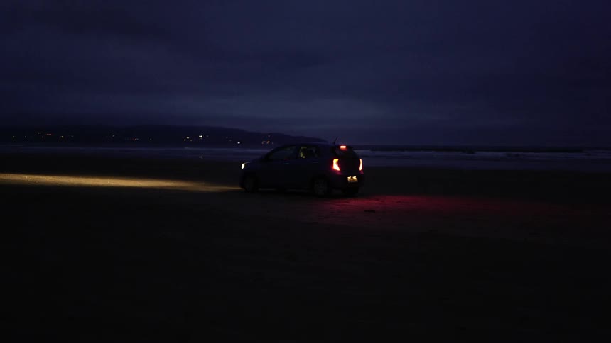 A car parked with its lights on near an ocean