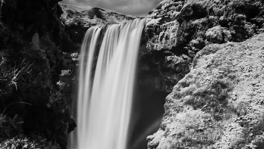 Water rushes over a cliff in a canyon into a river below