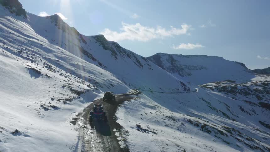 All terrain vehicles driving on a dirt road through the snow covered mountains