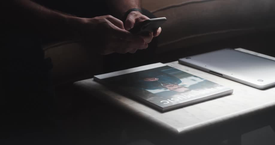 A person in a room sitting on a couch in front of a table using a smart phone