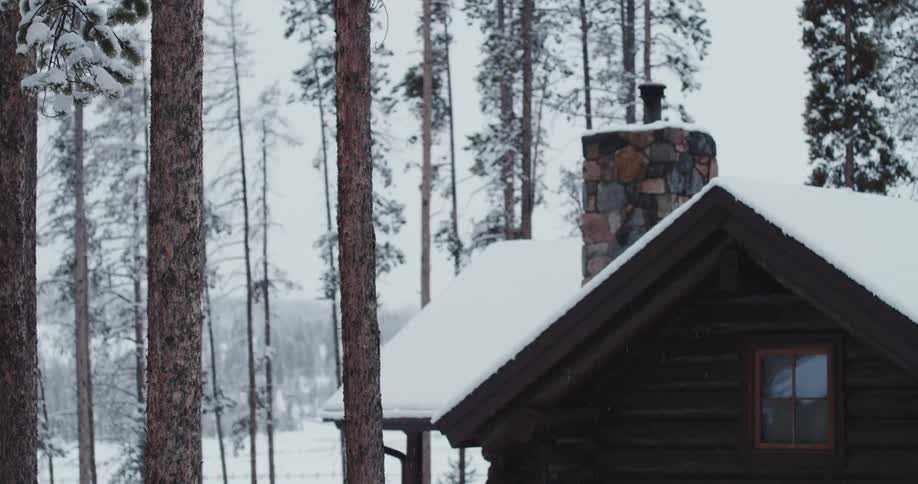 A cabin covered with snow with trees the sky and clouds in the background