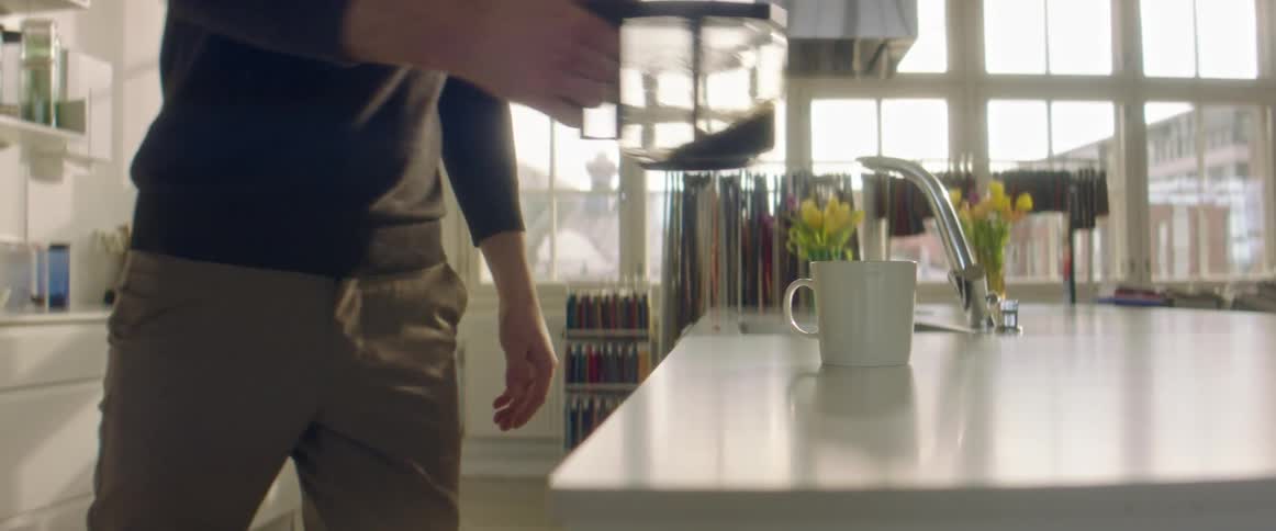 A man pours a cup of coffee in a large open kitchen space