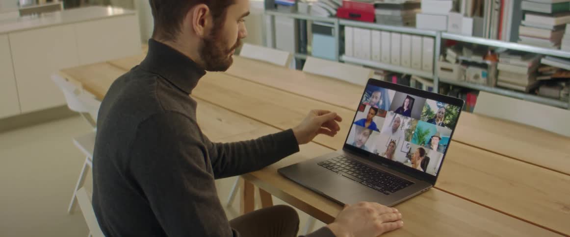 A man sits at a table with a laptop having a video call