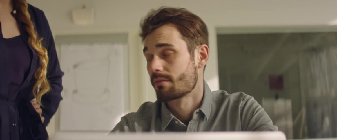 A man and a woman in a room looking at a laptop with a wall in the background