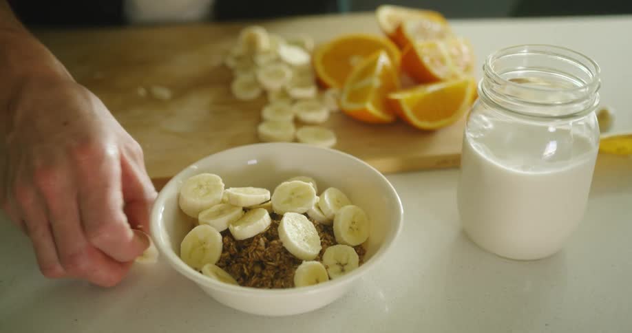 A woman puts bananas in to a bowl of cereal