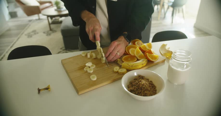 A person cuts a banana and other fruit on a cutting board