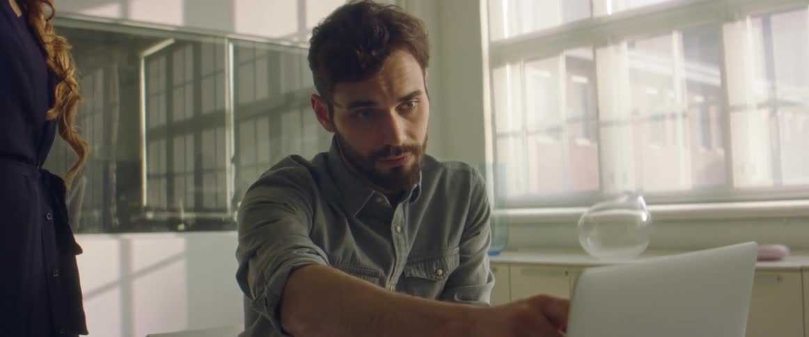 Coworkers discuss contents of laptop sitting on table in brightly lit room