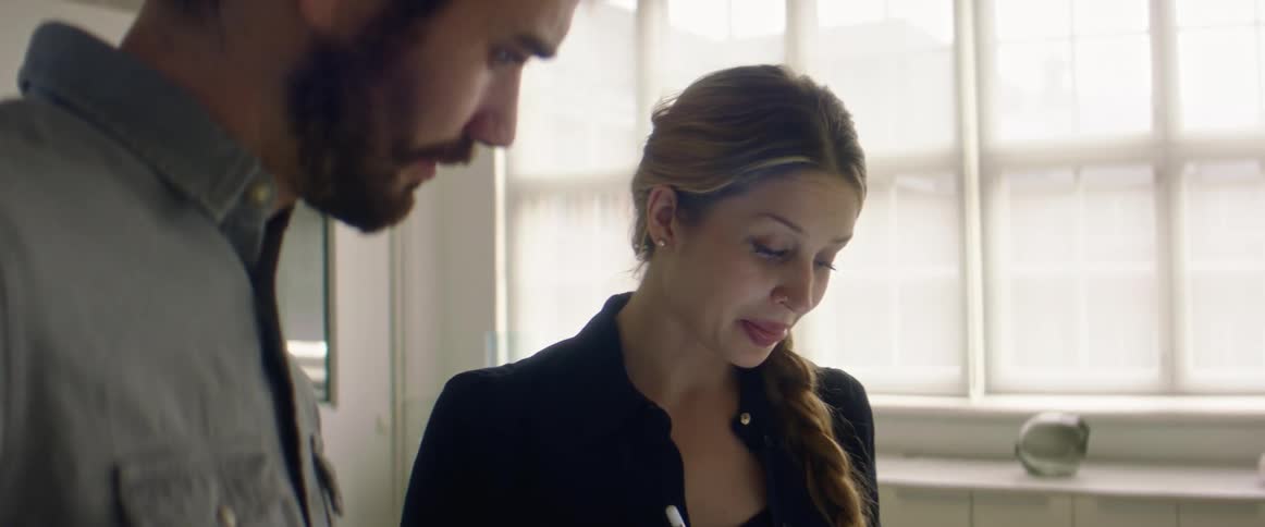 A man and a woman in a room looking at a tablet with a wall in the background