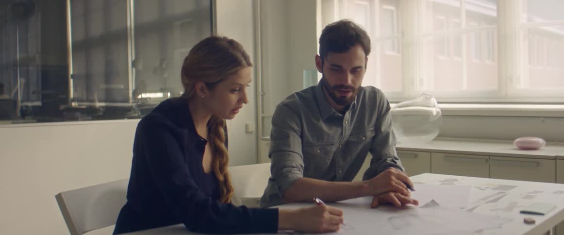 A man and woman sit together at a table writing and drawing on papers