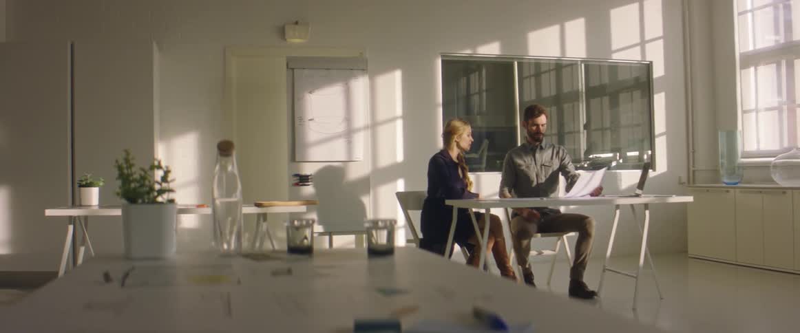 A man and a woman sitting on chairs at a desk and looking at a paper