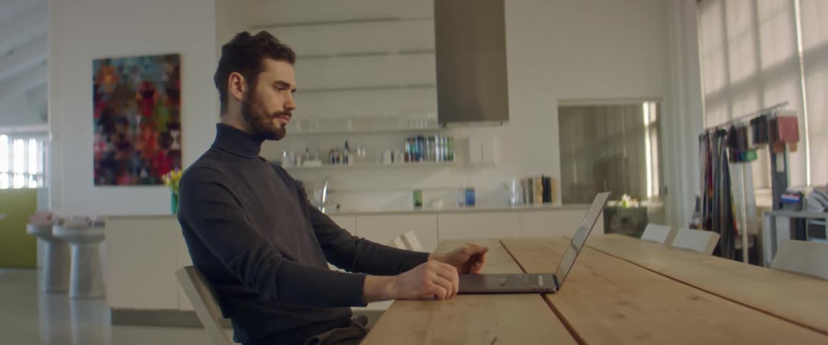 A man sits at a table with his open laptop and talks as he video chats