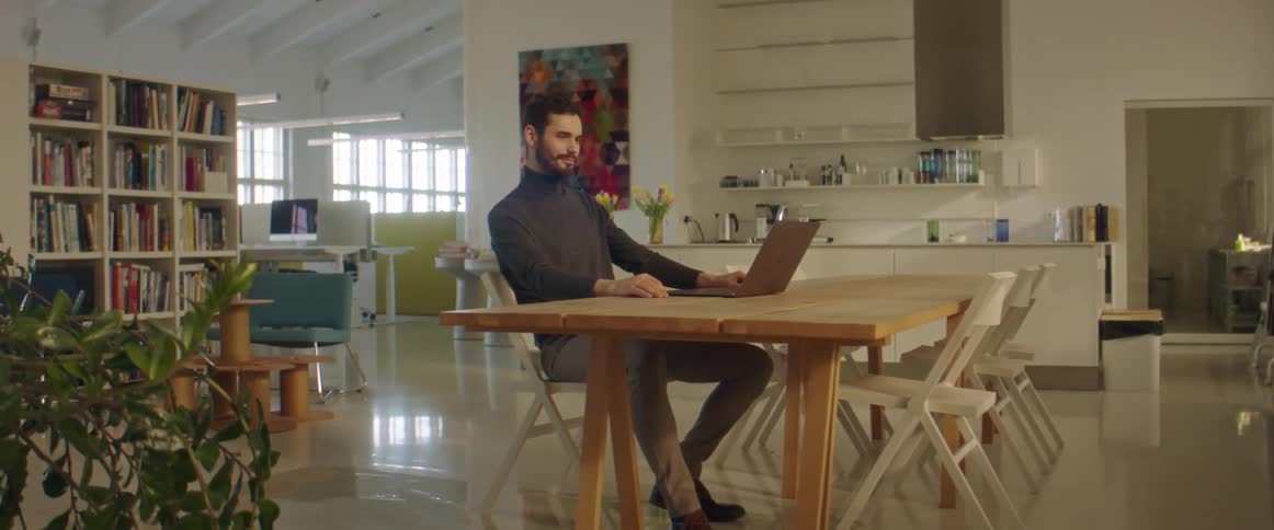 Bearded man working on a laptop in the cafeteria of an office