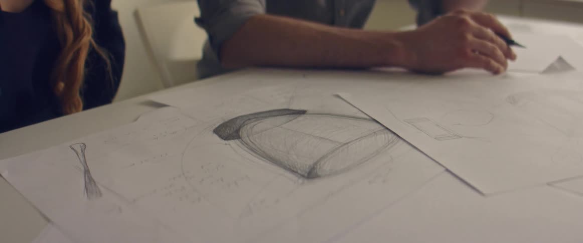 A man and woman sit together at a table covered in sketches
