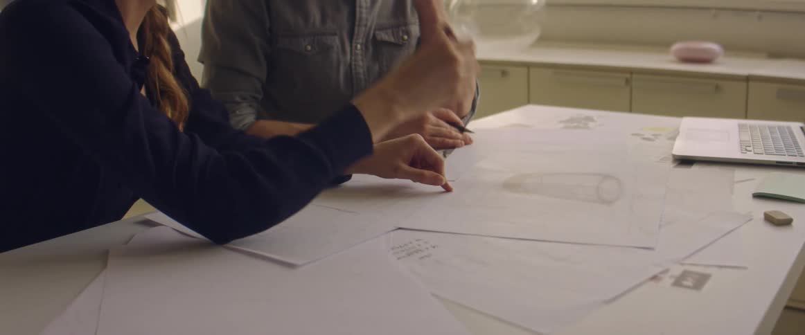 Coworkers drawing designs on paper over a desk in the office