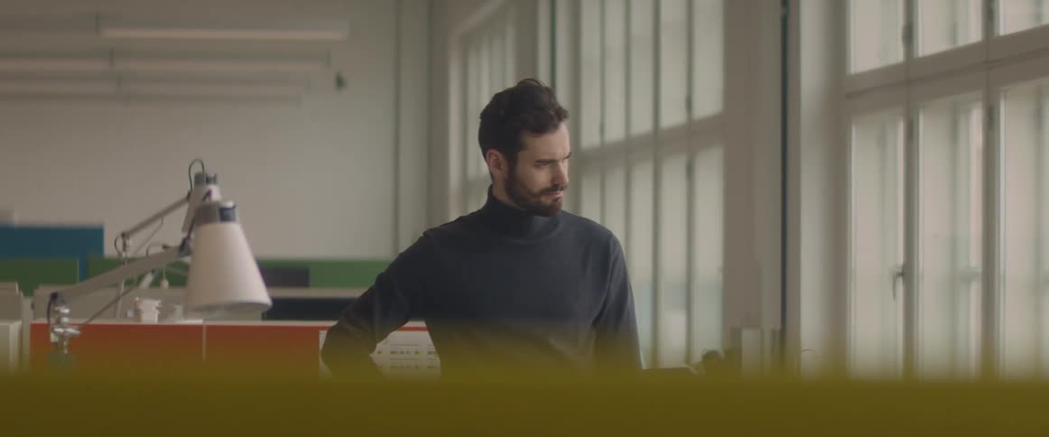 A man stands at an office cubicle space concentrating on something and looking out the window
