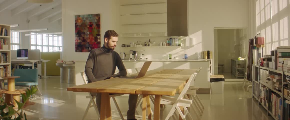 A man takes a video call on his laptop while sitting at a table in the library