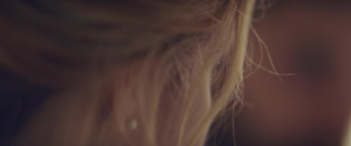 A woman in a room with a nose ring with a man and a wall in the background