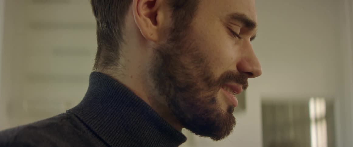 Bearded man smiles and nods as he talks while a piece of artwork is on the wall behind him