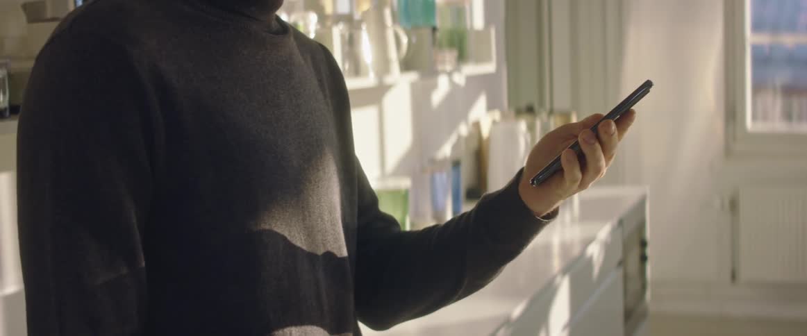 A man in his kitchen scrolls on his phone