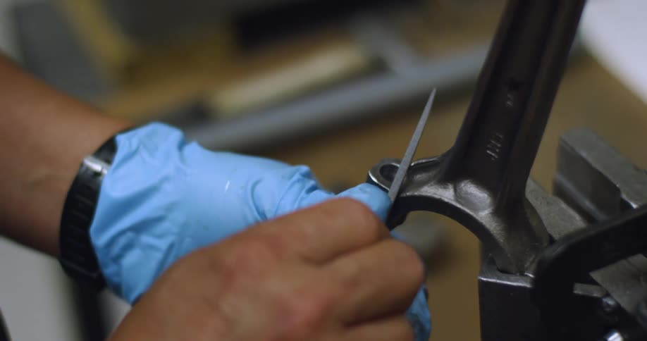 Man filing a metal piece over a workbench
