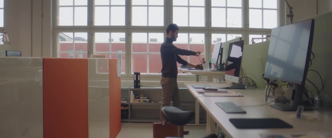 A man walks to an office computer station and places a laptop on the counter