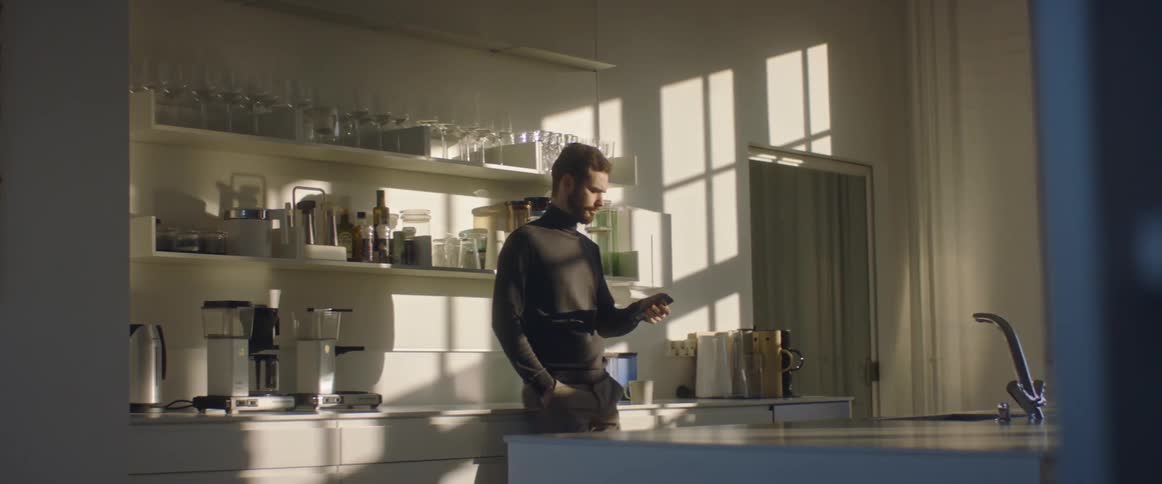 A man answers his phone while standing in his kitchen