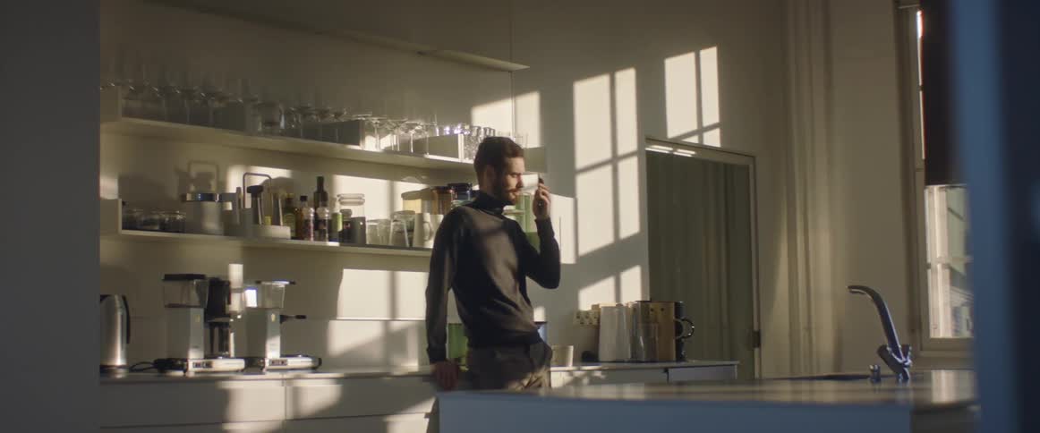 A man stands in a large home kitchen talking on his cell phone